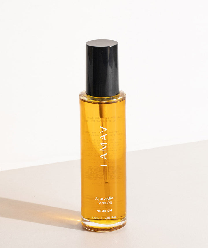 LAMAV Ayurvedic Body Oil Nourish glass bottle standing on a minimalist surface casting a shadow.