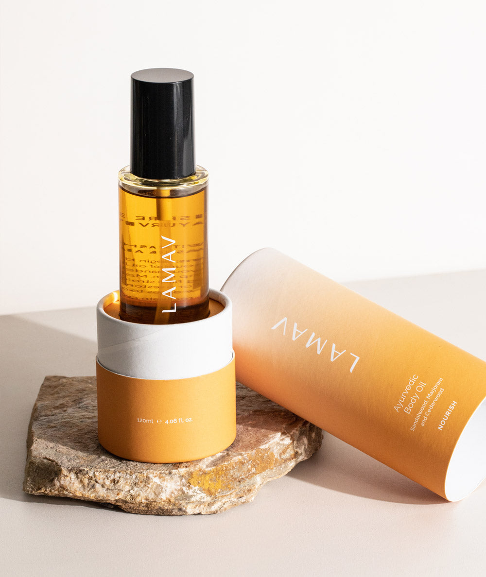 LAMAV Ayurvedic Body Oil Nourish resting in orange packaging on a natural stone. Hydrating skincare.