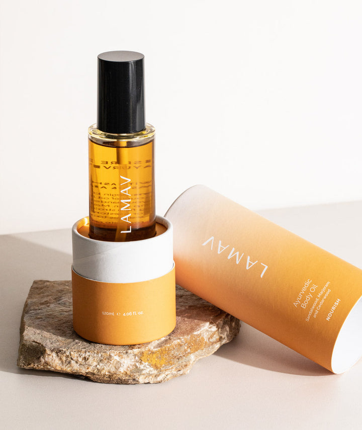 LAMAV Ayurvedic Body Oil Nourish resting in orange packaging on a natural stone. Hydrating skincare.