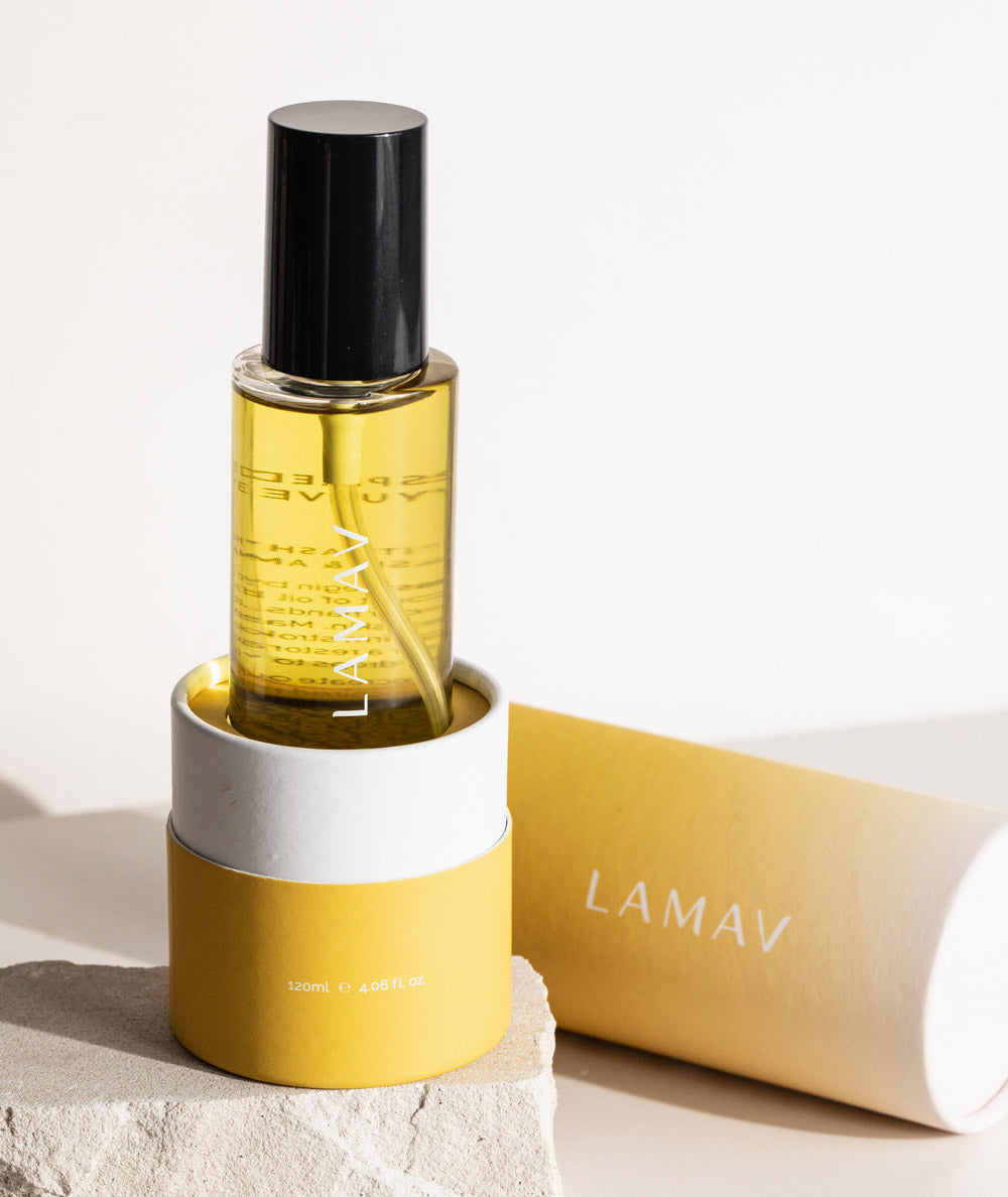 LAMAV Ayurvedic Body Oil Unwind in a yellow glass bottle resting on a stone display.