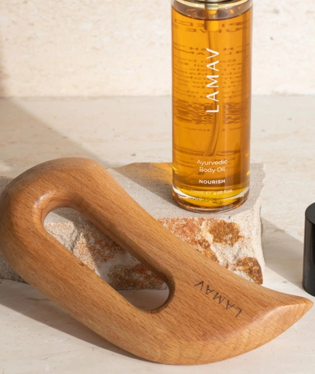 LAMAV Nourish Body Oil bottle and wooden Aura Gua Sha resting against a textured stone block.