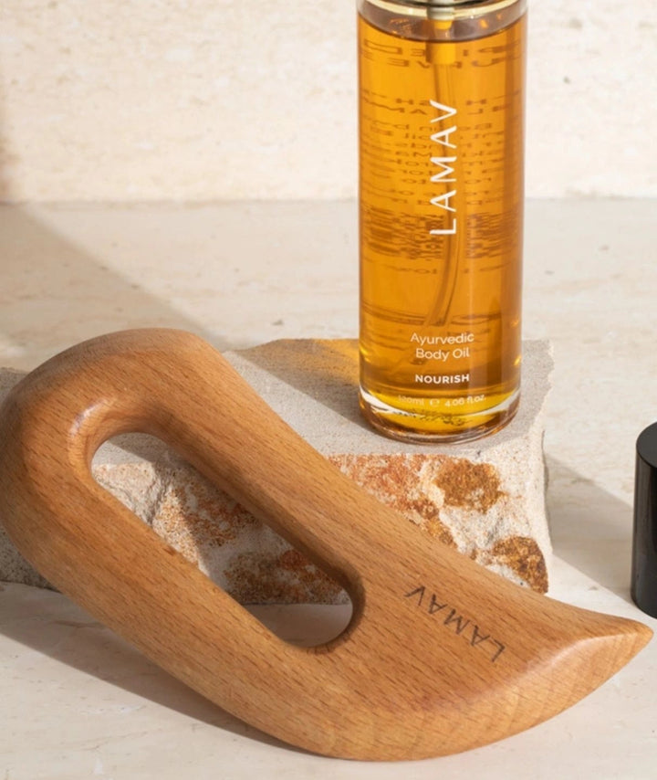 LAMAV Nourish Body Oil bottle and wooden Aura Gua Sha resting against a textured stone block.