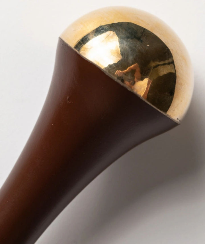 Extreme close-up of the LAMAV Ayurvedic Kansa Wand showing the smooth bronze dome and wooden handle for facial massage.