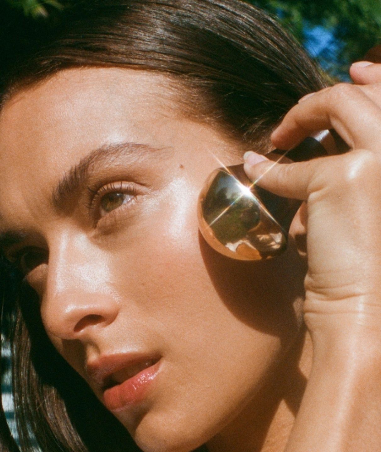 Woman outdoors using the LAMAV Ayurvedic Kansa Wand on her cheek to massage skin and promote a healthy facial glow.