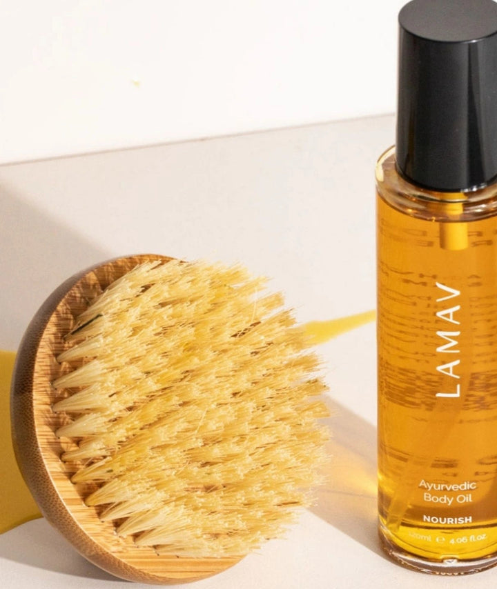 LAMAV dry body brush next to a bottle of LAMAV Nourish Ayurvedic Body Oil.