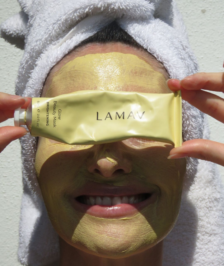 Model holding LAMAV Glow Beauty Mask 60ml, a natural brightening face mask formulated to improve skin tone, boost radiance