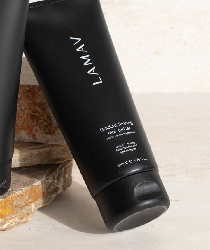 LAMAV Gradual Tanning Moisturiser resting against stacked natural stones. Hydrating gradual tan lotion.