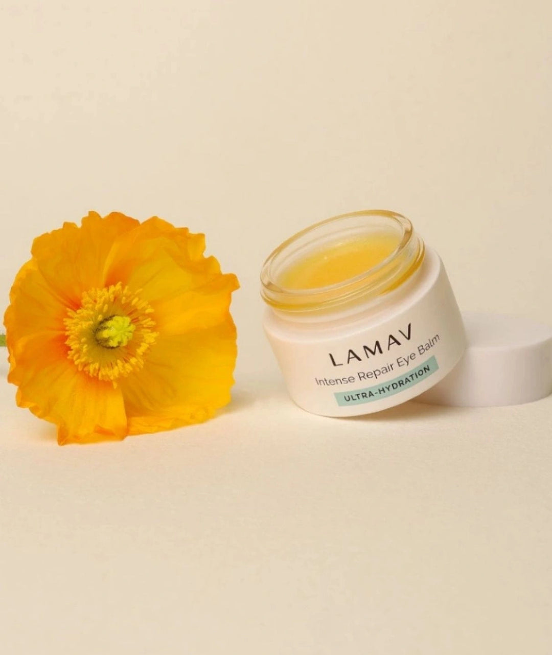 Open LAMAV Intense Repair Eye Balm jar next to a yellow flower. Natural ultra-hydration eye skincare.