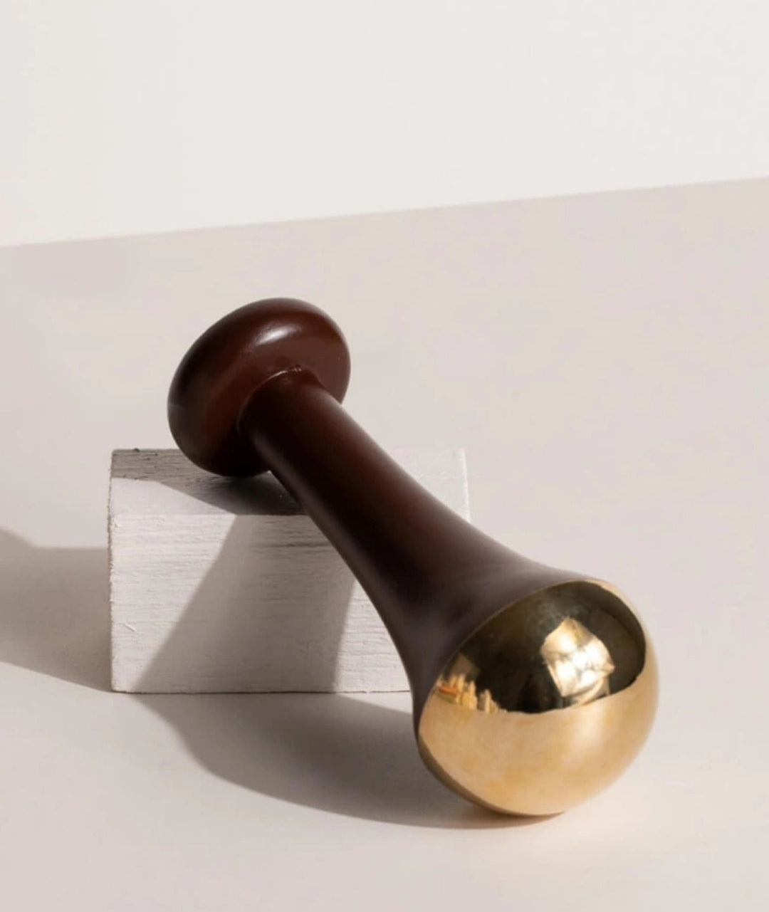 LAMAV Ayurvedic Kansa Wand resting on a white textured display block. Traditional wooden and bronze facial massage tool.