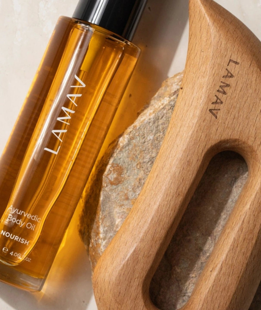Close up of LAMAV Nourish Ayurvedic Body Oil and wooden Aura Body Gua Sha on a natural stone.