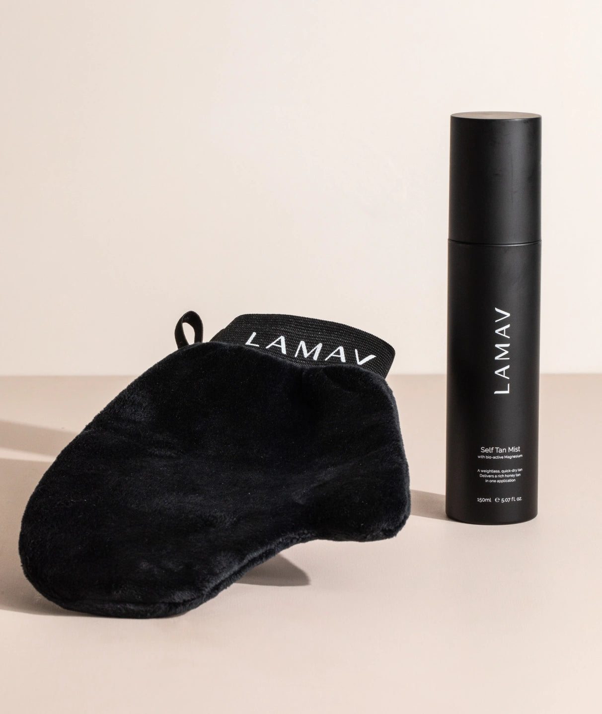LAMAV Self Tan Mist and application mitt standing on a minimalist beige surface. Natural sunless tanning.
