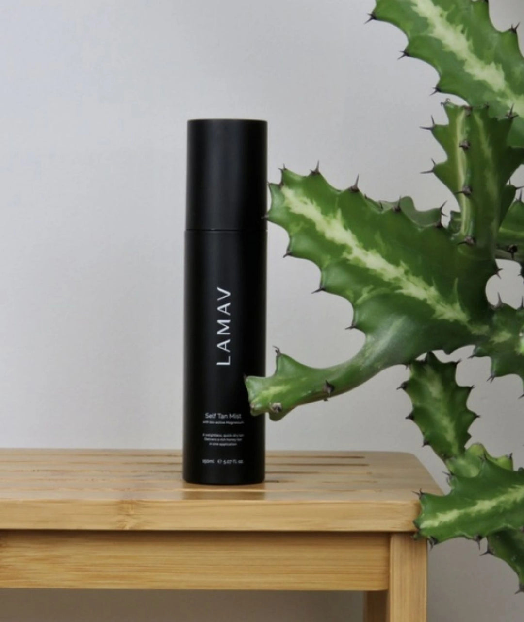 LAMAV Self Tan Mist with bio-active magnesium on a wooden bench next to a green plant.