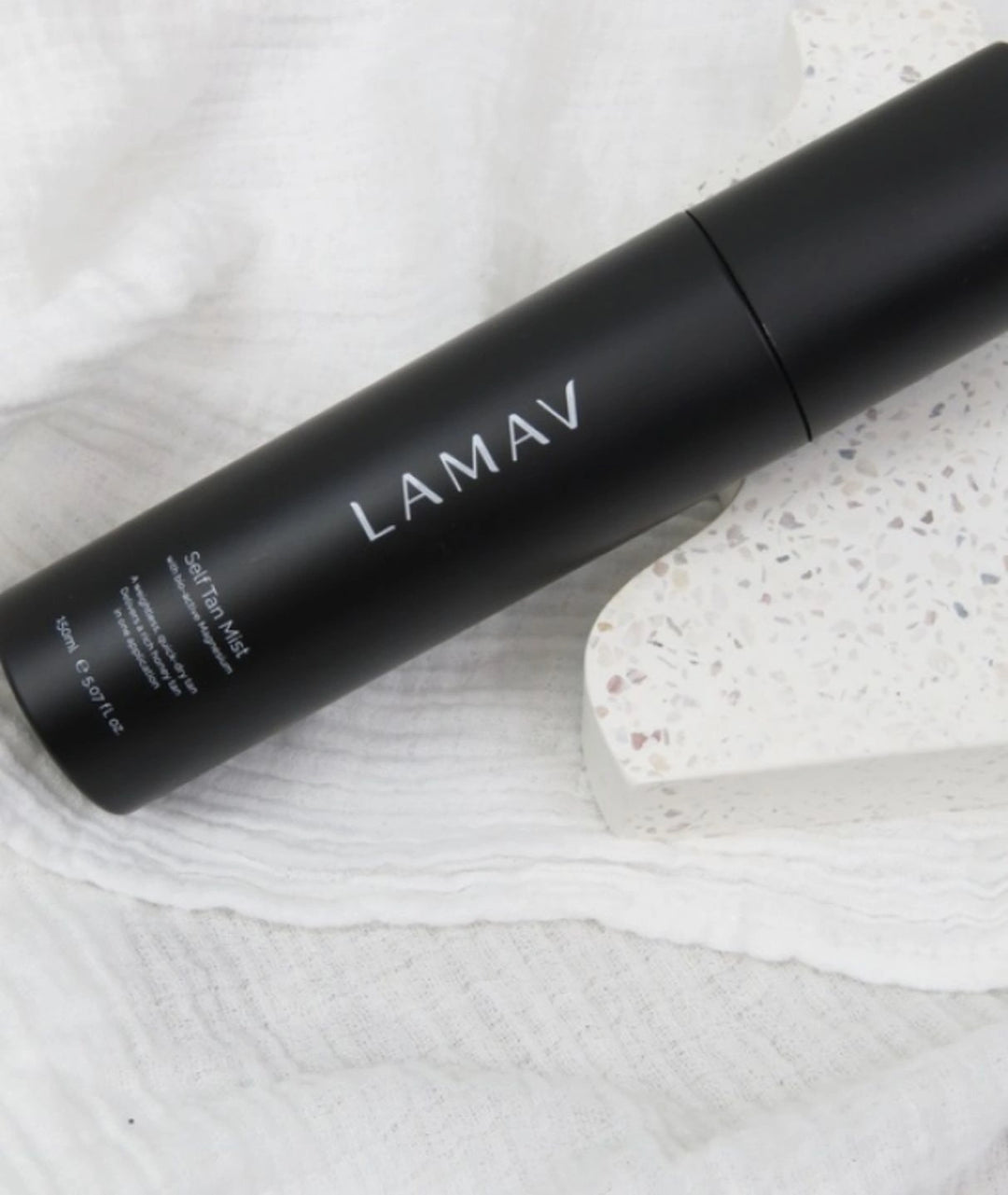 LAMAV organic self tanning mist resting on a terrazzo stone and white muslin cloth.