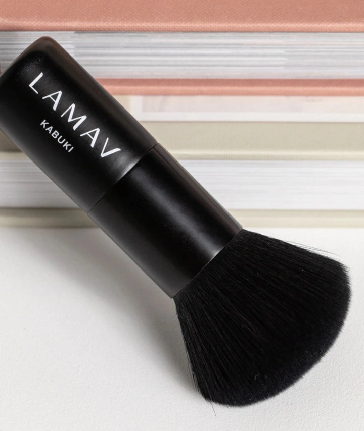 LAMAV Vegan Kabuki Brush resting flat with books in the background. Eco-friendly makeup blending tool.