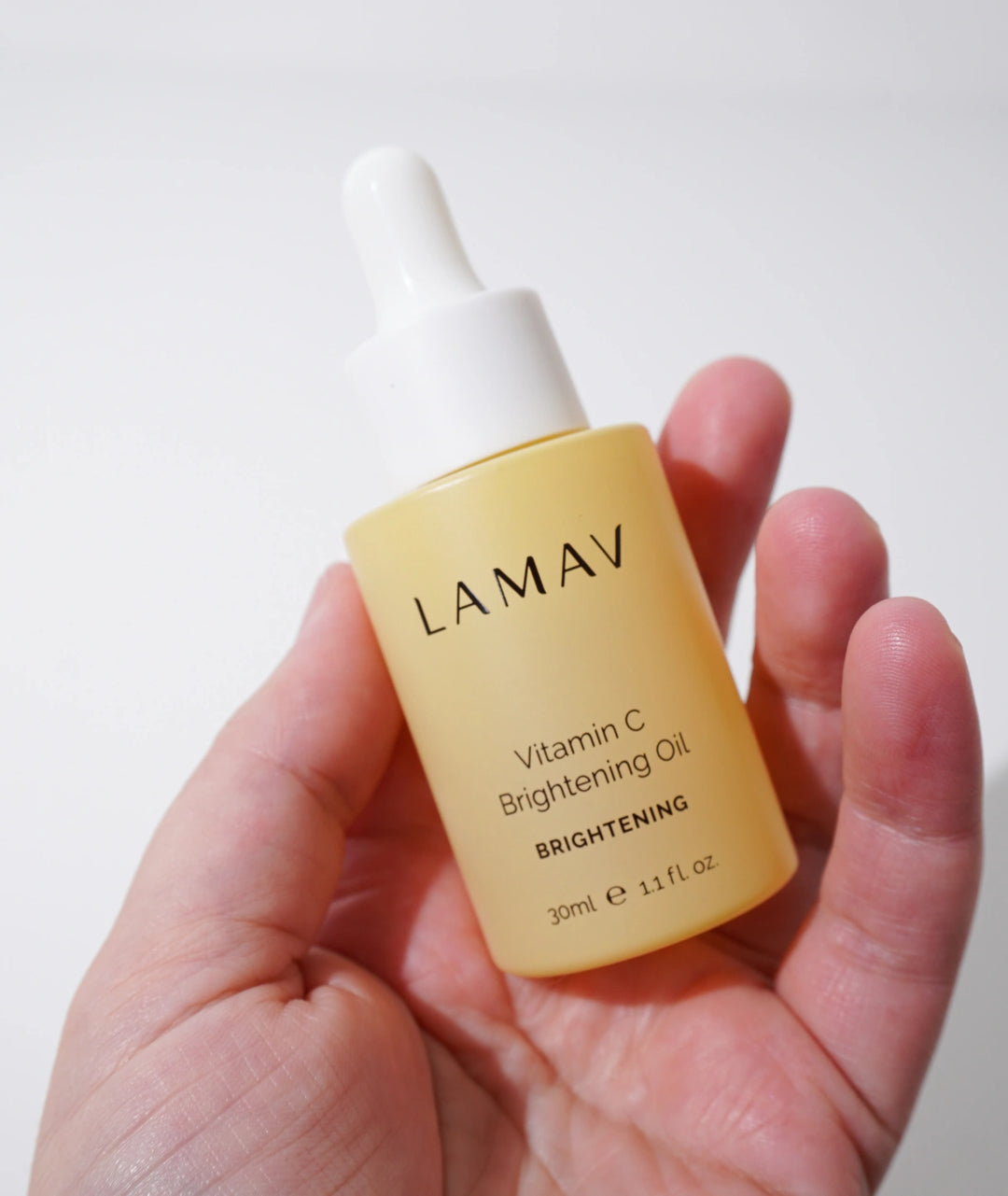 Hand holding LAMAV Vitamin C Brightening Oil 30ml. Natural brightening skincare serum in a yellow bottle.