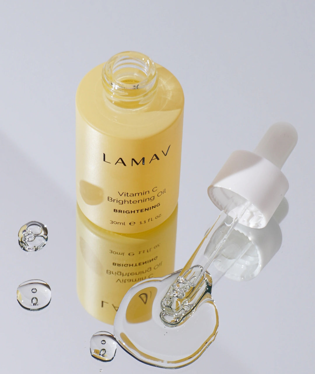 Open LAMAV Vitamin C Brightening Oil 30ml with glass dropper and serum drops on a reflective surface.