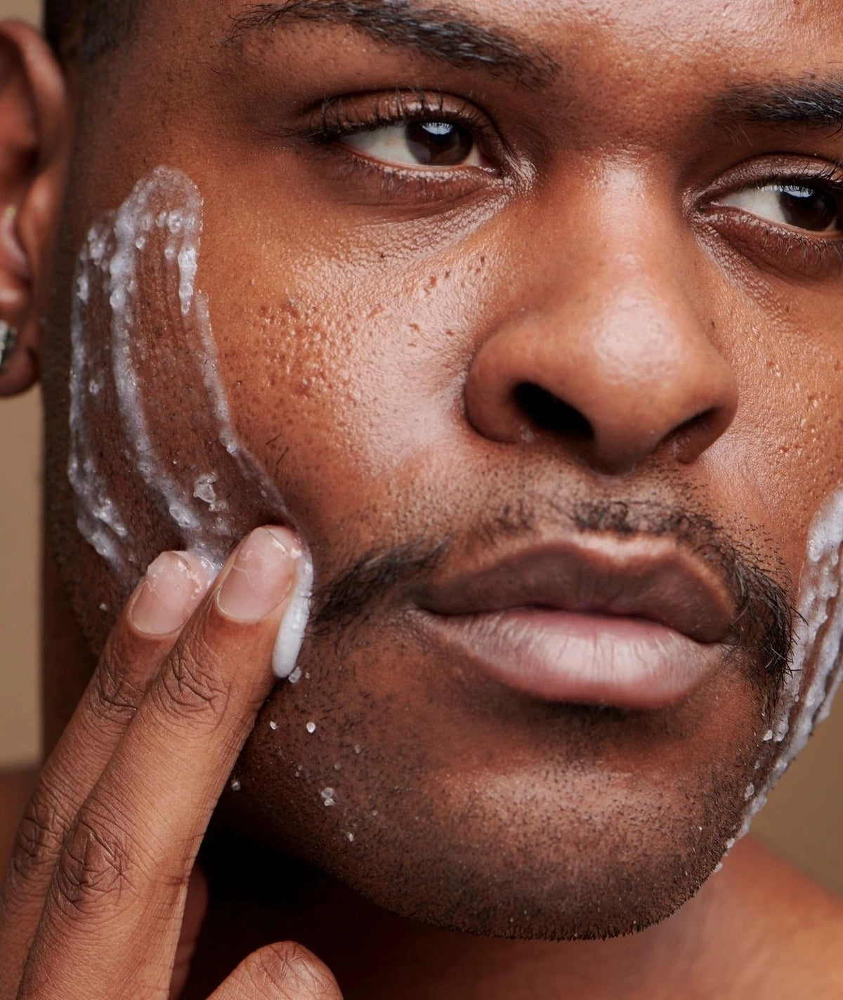 Close-up of a man massaging the LAMAV AHA Face Exfoliant into his cheek for smooth skin