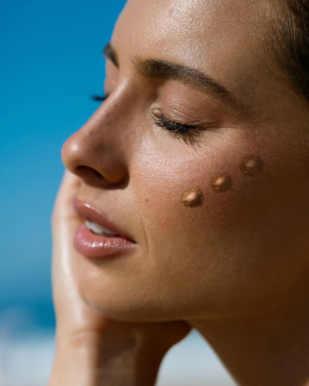 Model wearing Mother SPF Mother of Pearl Bronzing Drops with bronzing drops applied to the cheek, creating a natural radiant glow and healthy sun-kissed complexion.