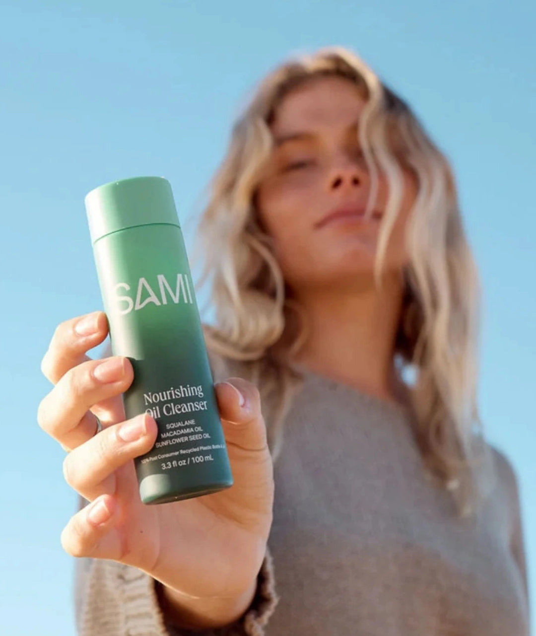 Model holding SAMI Nourishing Oil Cleanser 100ml green bottle outdoors for daily skincare.