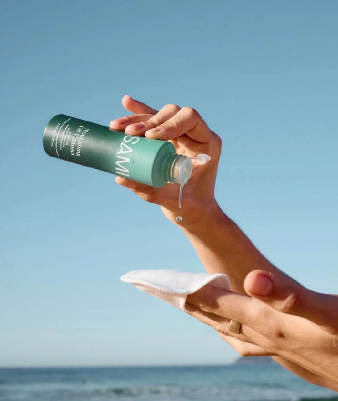 Hands pouring SAMI Nourishing Oil Cleanser onto reusable cotton pad for gentle facial cleansing.