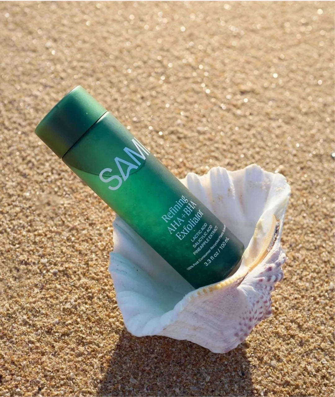 Refining AHA BHA Exfoliator by SAMI — green bottle resting inside a seashell on the beach sand | Gently smooths the skin