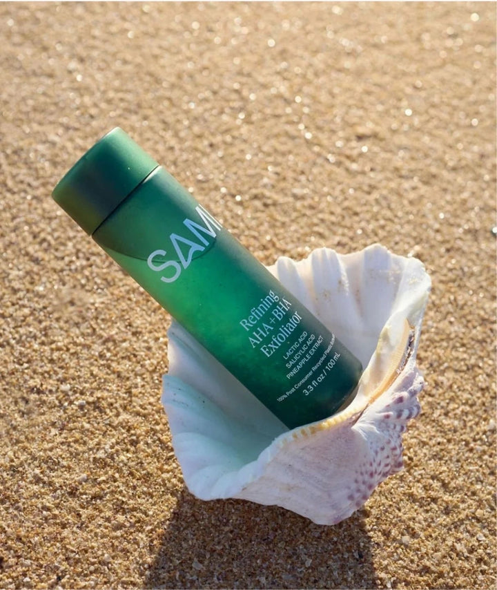 Refining AHA BHA Exfoliator by SAMI — green bottle resting inside a seashell on the beach sand | Gently smooths the skin
