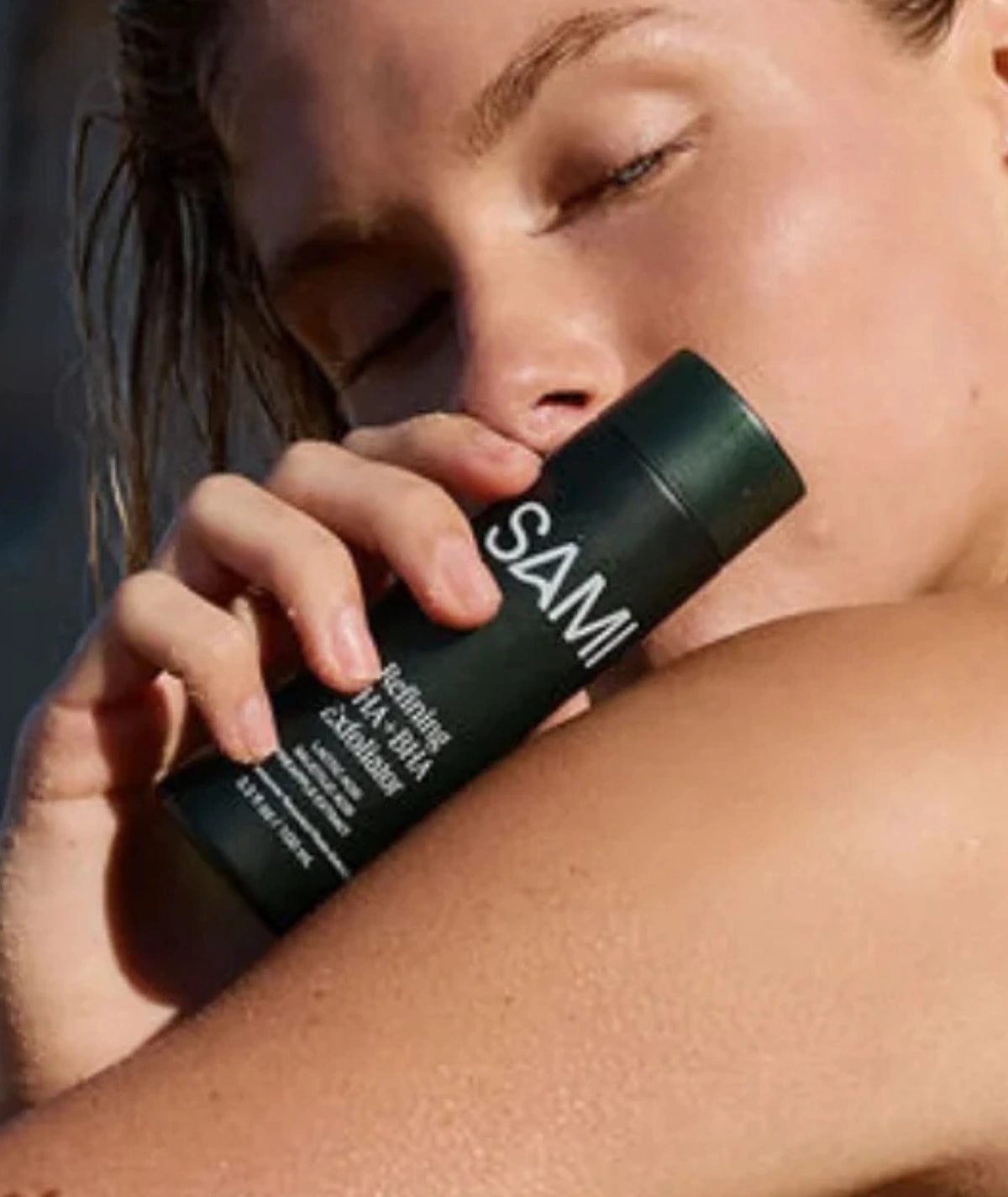 Refining AHA + BHA Exfoliator by SAMI — woman holding dark green bottle against radiant skin
