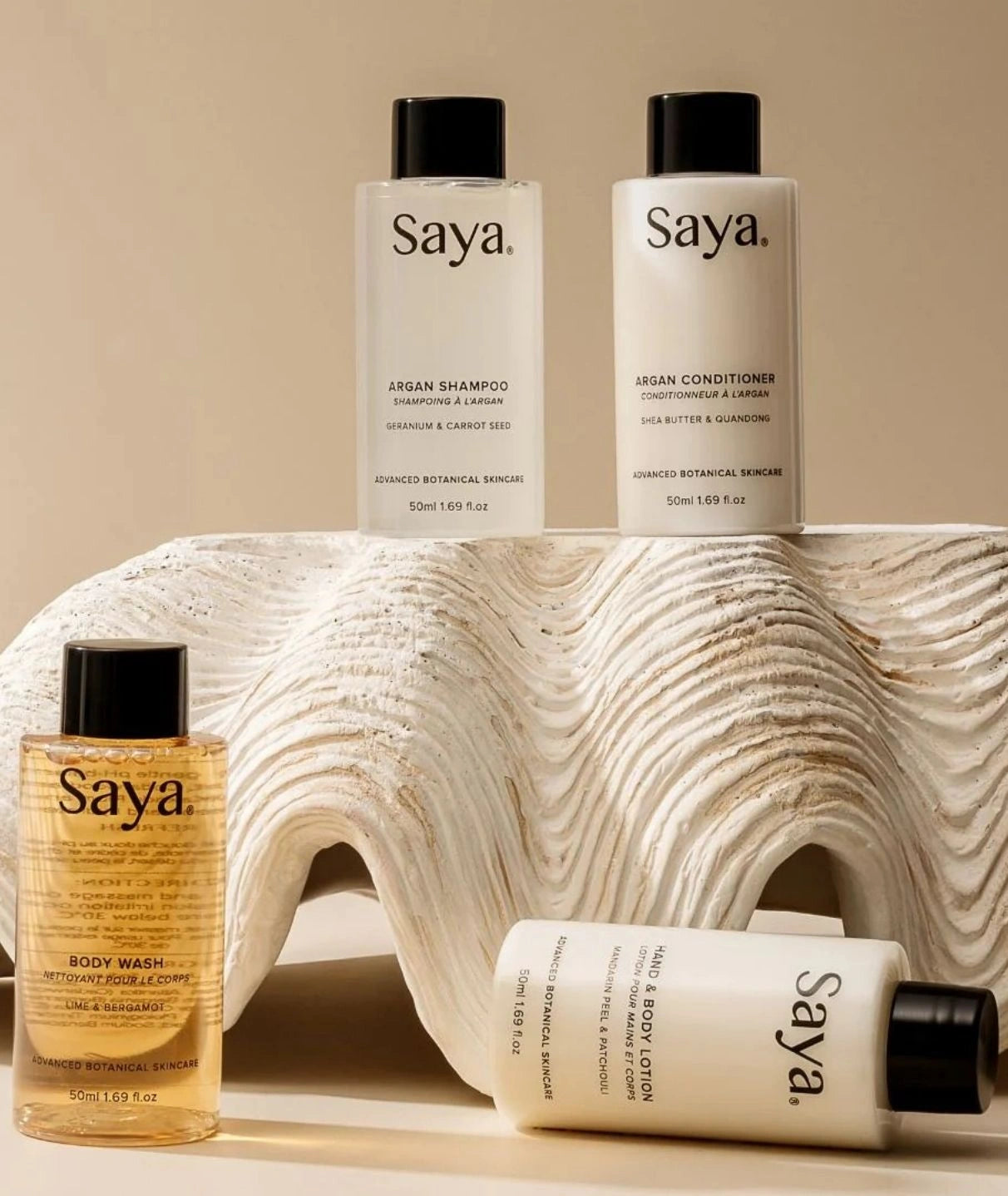 Saya botanical skincare travel bottles including Argan Conditioner displayed on a decorative white shell prop.