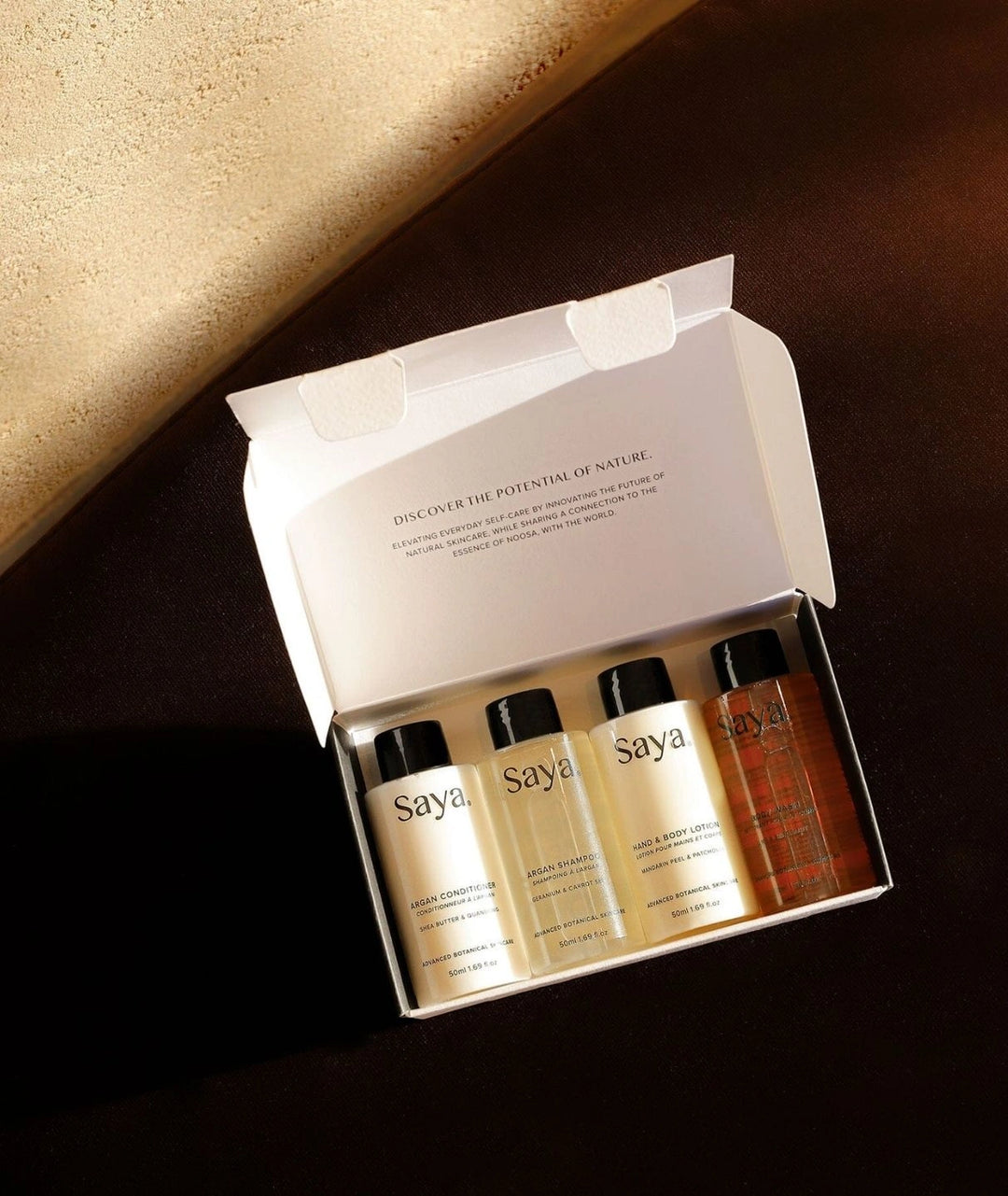 Saya Skincare travel set with Argan haircare and botanical body wash in an open box on a dark brown surface.