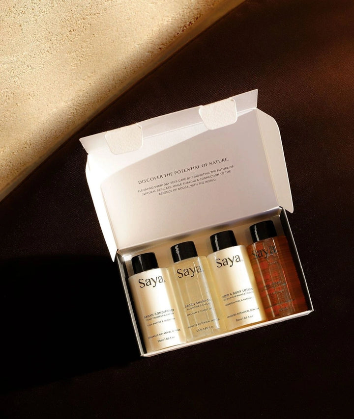 Saya Skincare travel set with Argan haircare and botanical body wash in an open box on a dark brown surface.