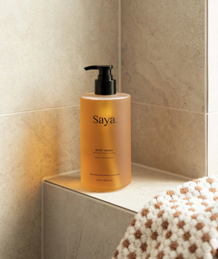 500ml Saya Lime & Lemongrass Body Wash resting on a stone shower ledge next to a woven towel.