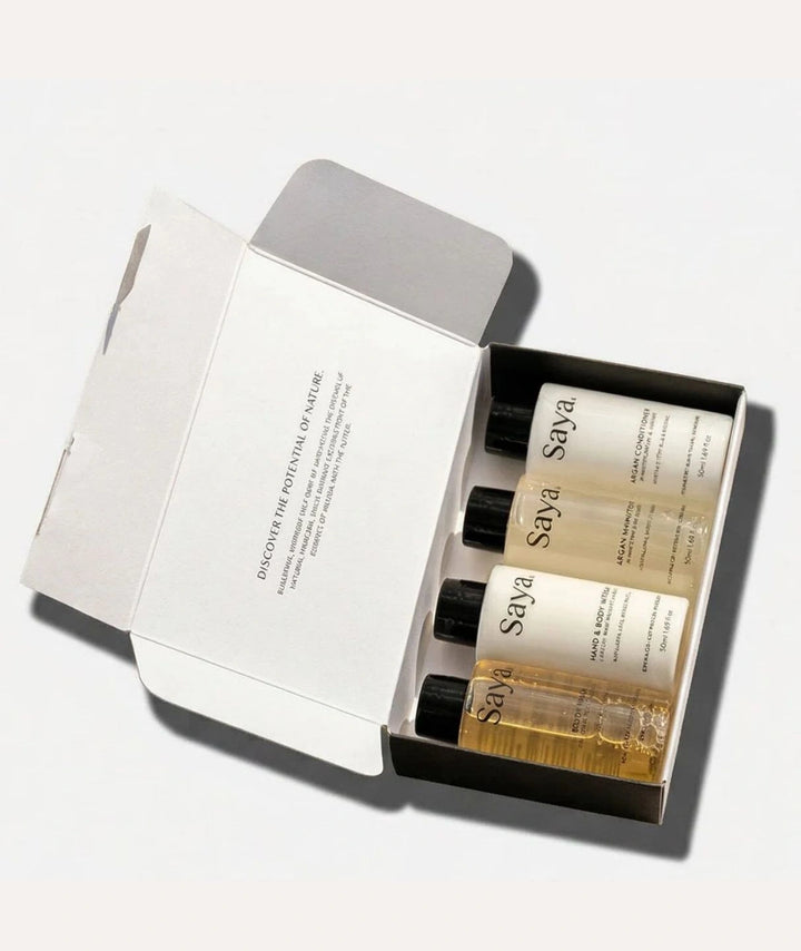 Open Saya Destination Essentials box revealing travel-sized Argan shampoo, conditioner, body wash, and lotion.