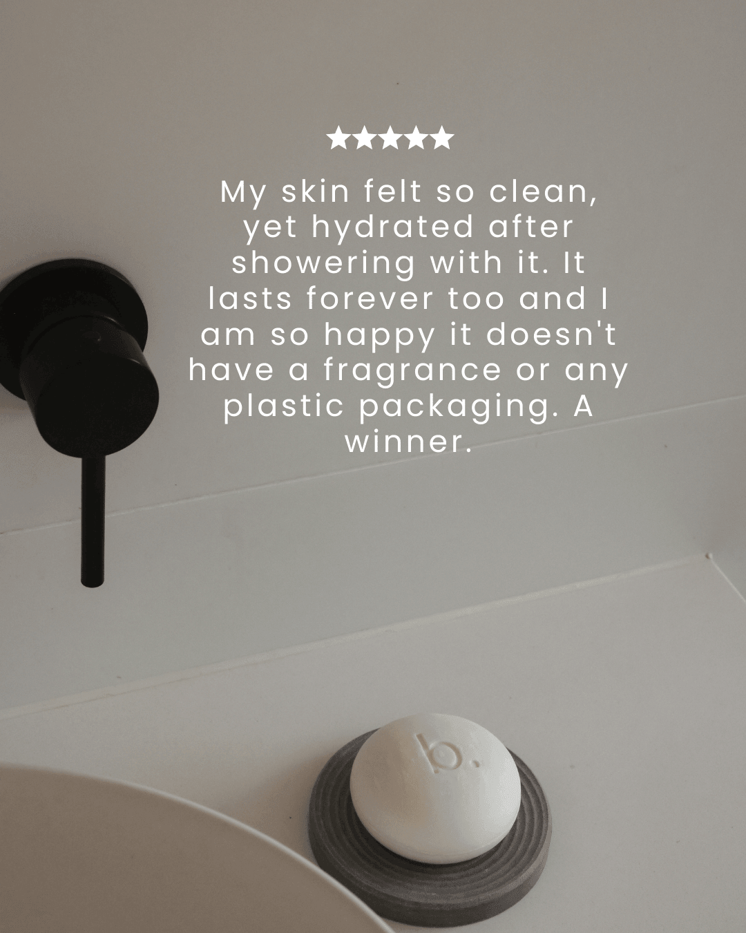 White soap bar on a gray soap dish with a black faucet in the background, featuring a five-star rating and customer review text.