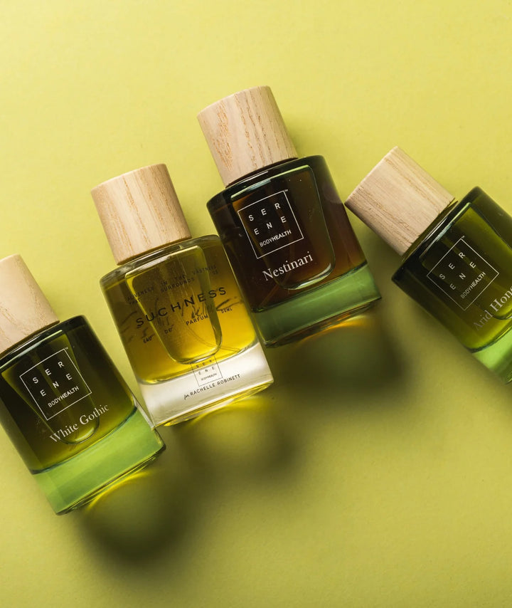 Serene Bodyhealth fragrance collection including White Gothic, Suchness, and Nestinari bottles on a green background.