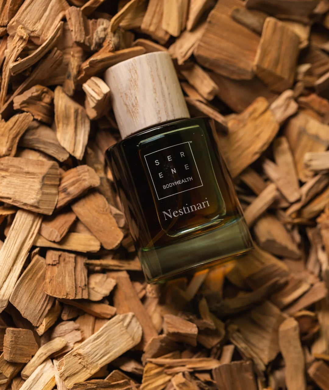 Serene Bodyhealth Nestinari perfume bottle with wooden cap resting on natural wood chips.