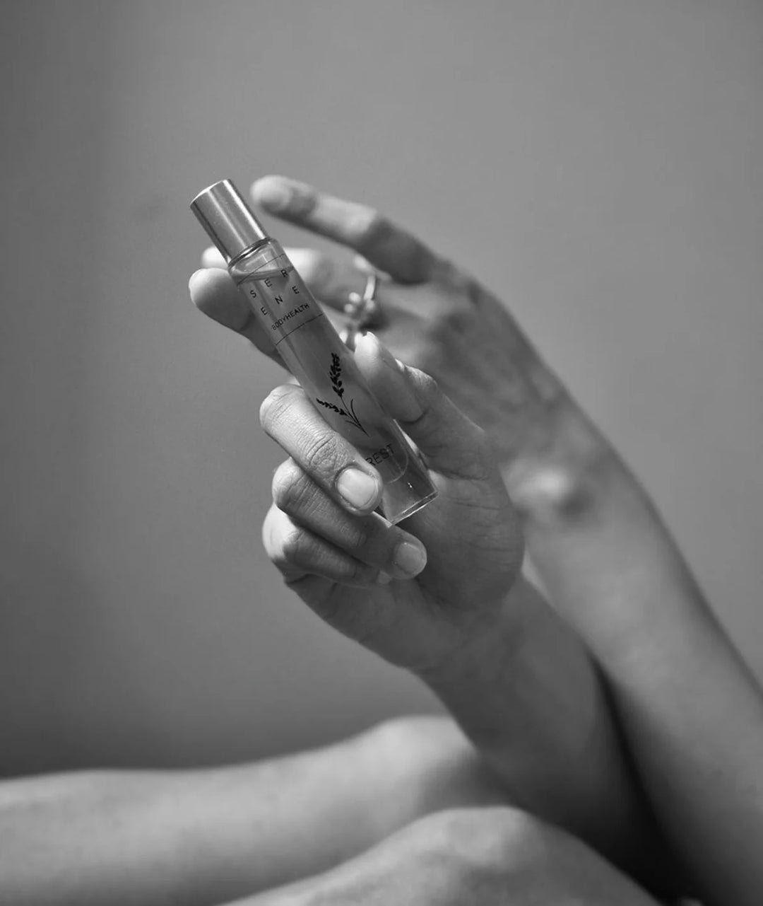 Close-up of hand holding elevated Serene Bodyhealth Rest essential oil perfume rollerball bottle.