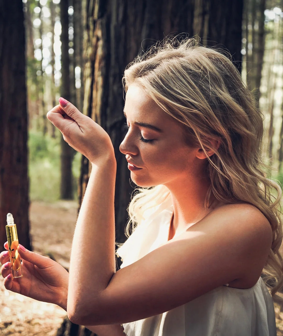 Woman smelling wrist after applying Serene Bodyhealth Lift essential oil perfume in a forest.