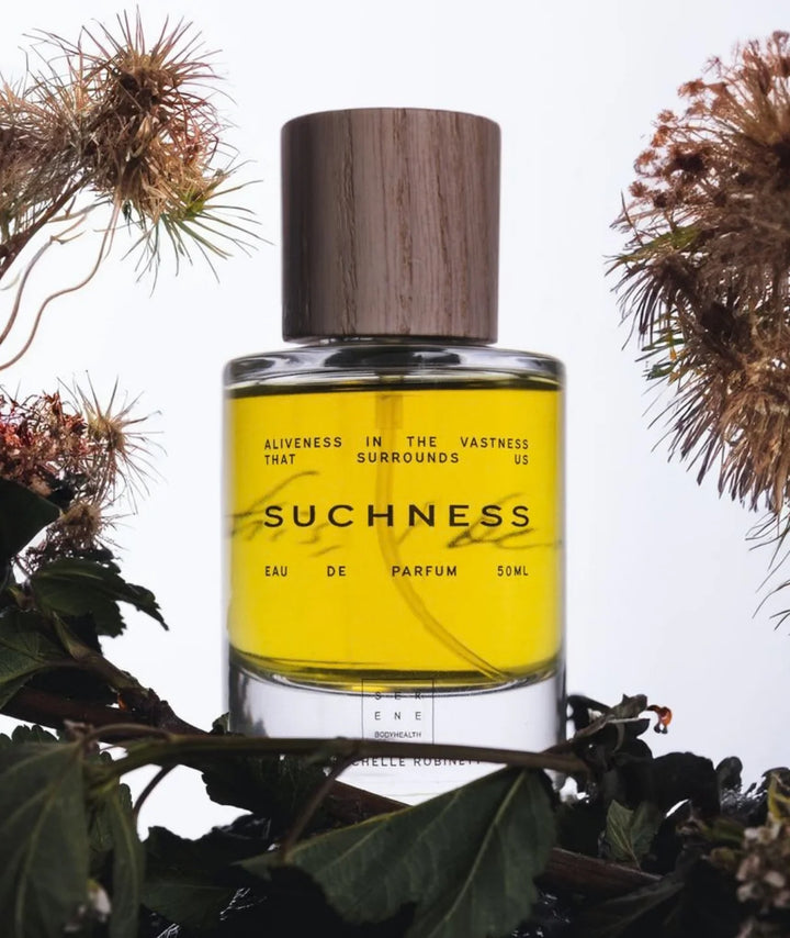 Suchness Eau de Parfum 50ml bottle by Serene Bodyhealth framed by natural botanical foliage and thistles.