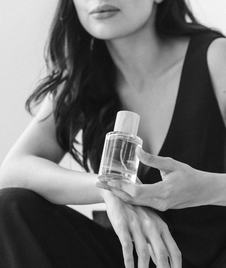 Black and white photo of a woman holding Serene Bodyhealth Suchness Eau de Parfum bottle with a wooden cap.