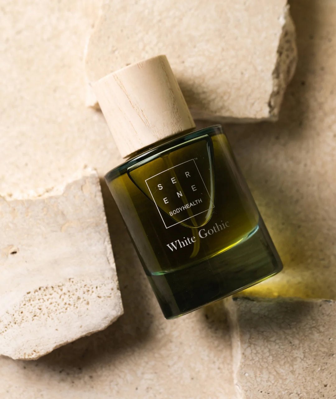 White Gothic fragrance by Serene Bodyhealth — elegant bottle resting on natural, textured beige stone blocks.
