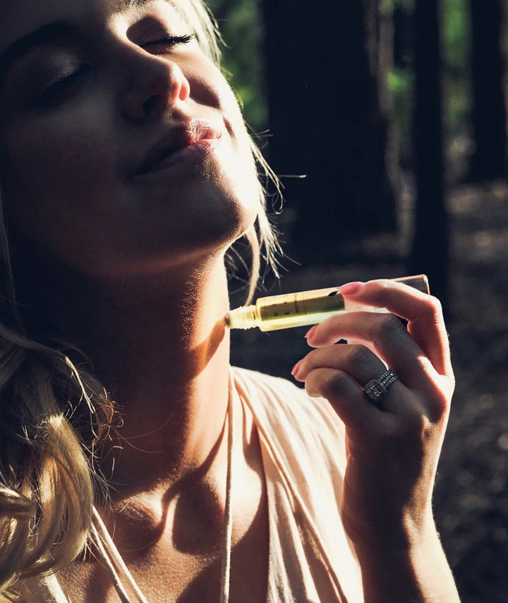 Woman applying Serene Bodyhealth Lift essential oil perfume rollerball to her neck outdoors.