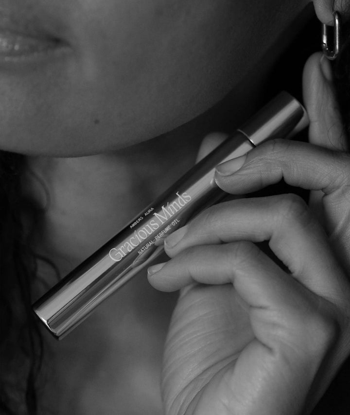 Woman holding Gracious Minds Ambers Aura natural perfume oil in a metallic roller.