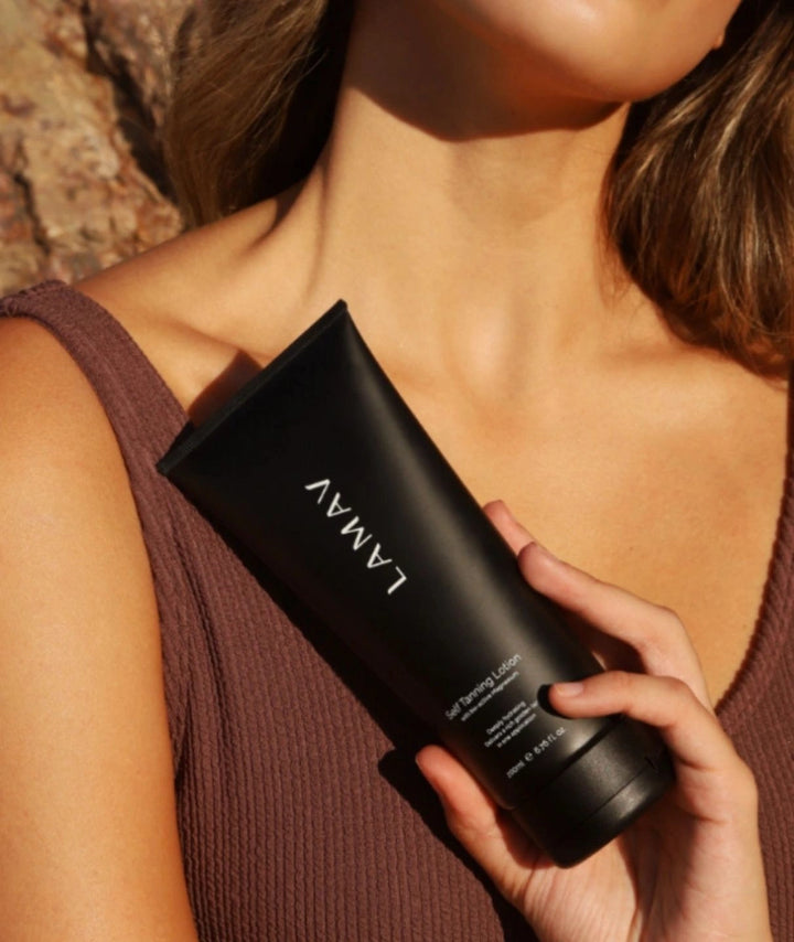 Woman outdoors holding LAMAV natural self tanning lotion against her glowing skin.