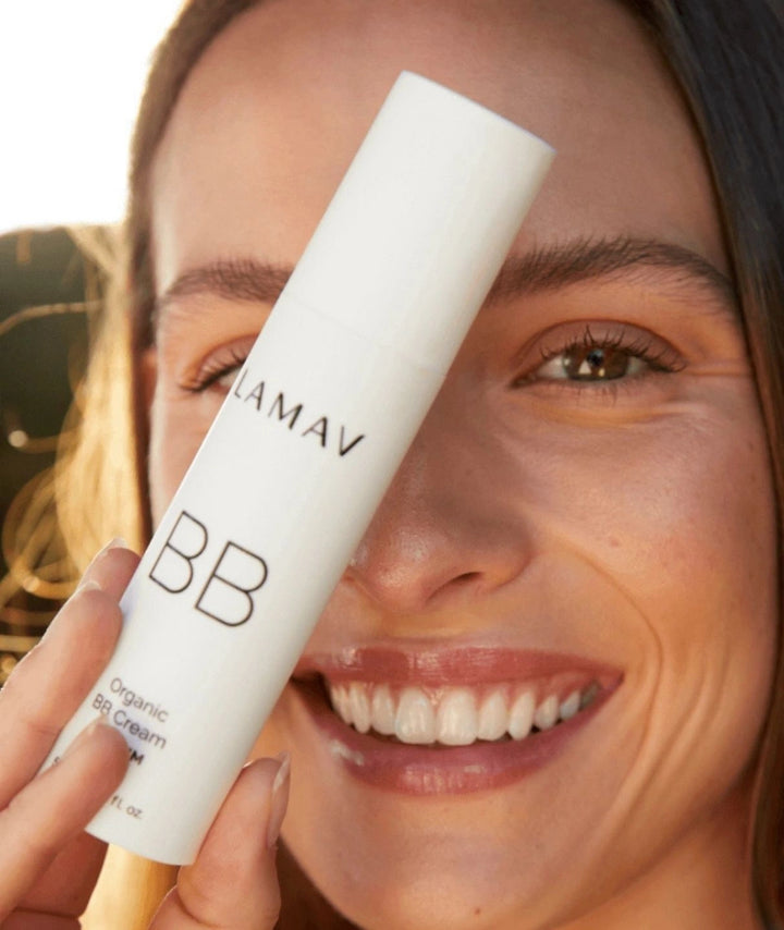 Smiling woman holding a bottle of LAMAV Organic BB Cream near her face.
