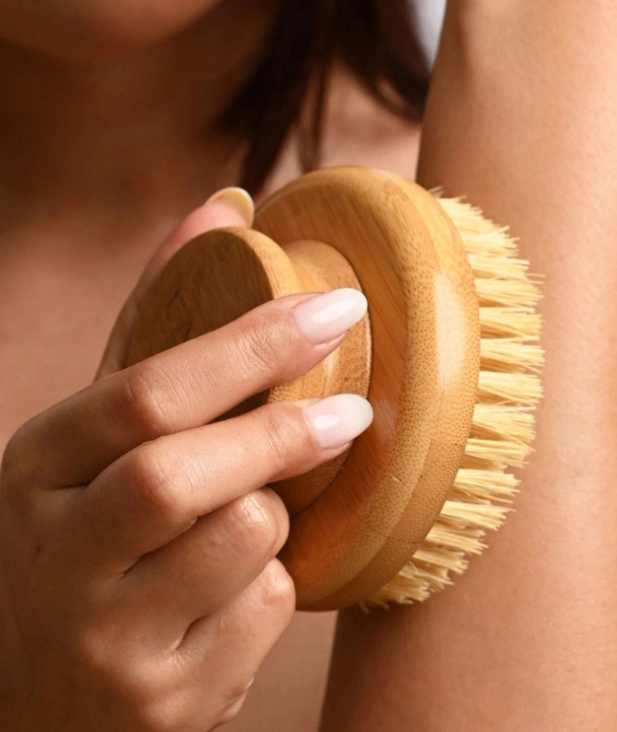 Woman using a round wooden LAMAV dry body brush to exfoliate her arm.